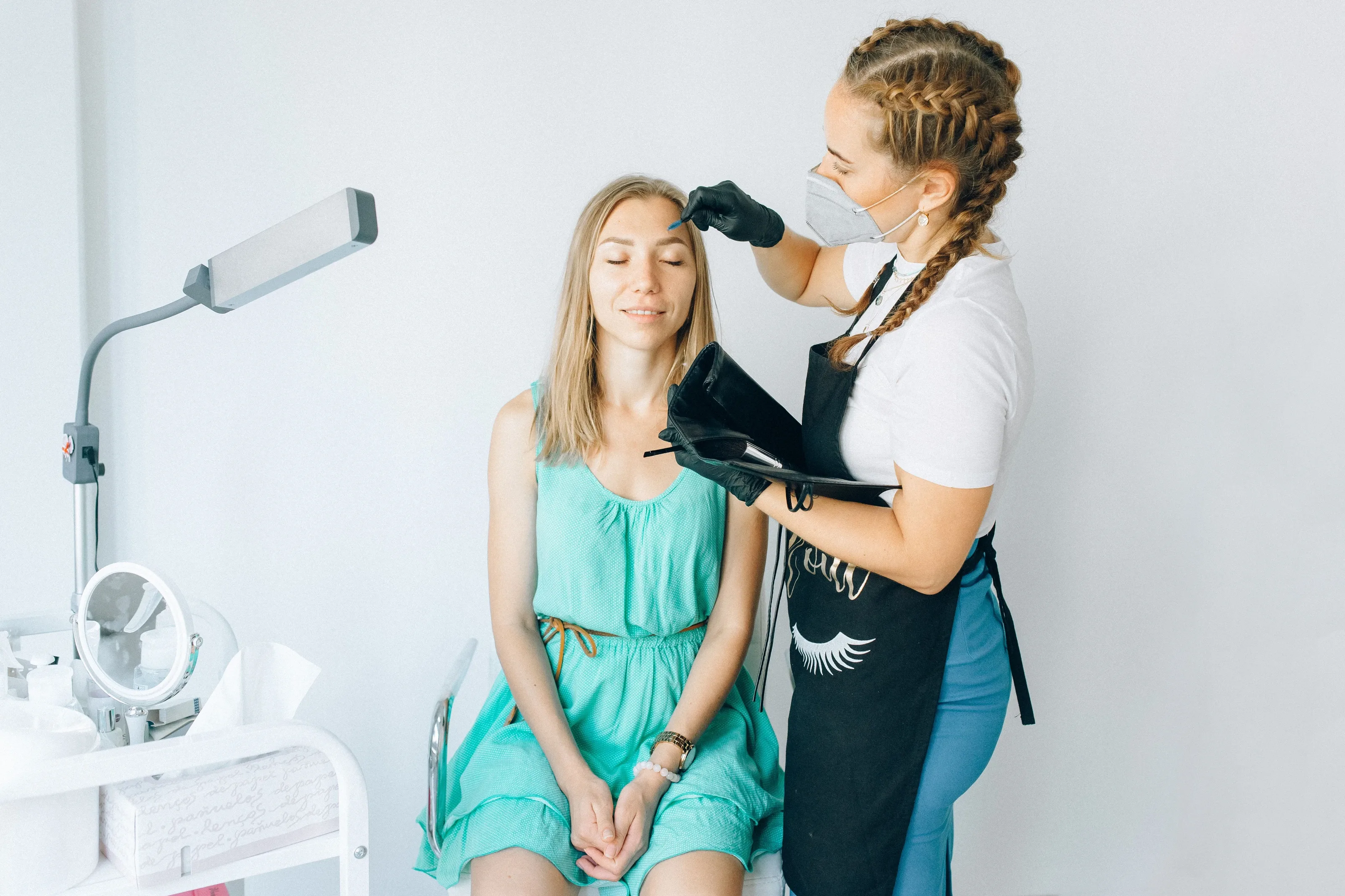 Brow artist applying a treatment to a seated client in a bright studio with a ring light