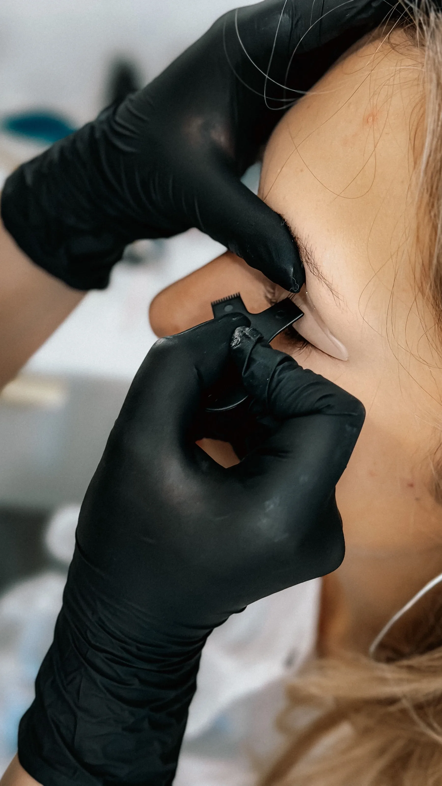 Gloved hands holding a fine tool beside a client's eyebrow