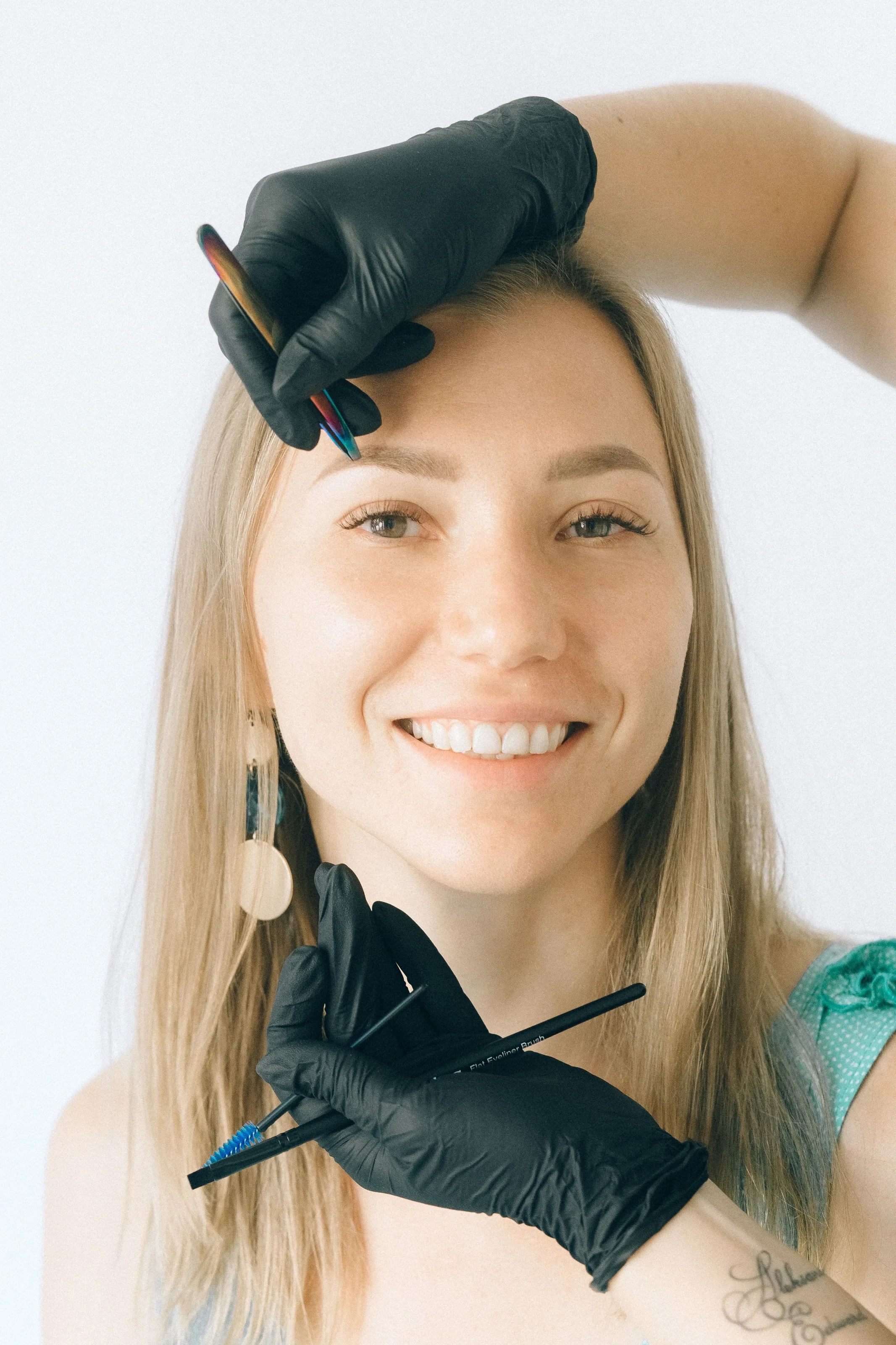 Smiling client having her eyebrows treated by a technician in black gloves